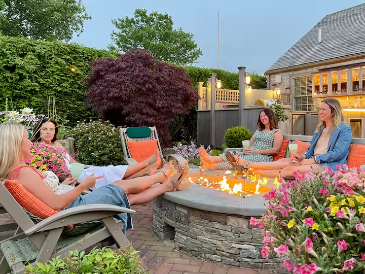 The Crew fire pit at dusk, with chairs gathered around the stone flame bar on herringbone brick.